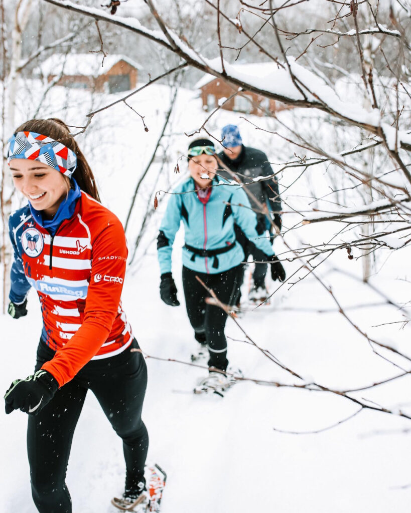 Three happy individuals walk through a snow-covered forest.