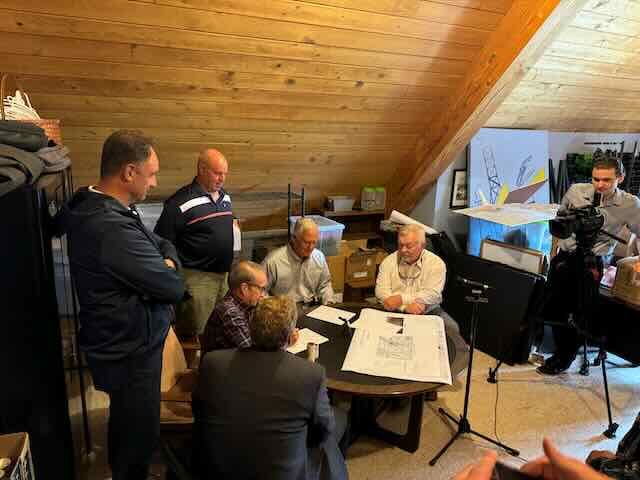 Dignitaries sitting around a table signing documents and looking on, being filmed while doing so